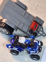 Blue ATV with rider and gray trailer overview