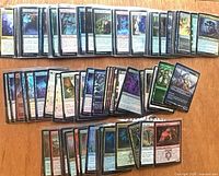 Two rows of sleeved foil MTG cards spread on table, showing variety of colors and card types