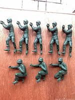 Eight green plastic toy soldiers on wooden background, full group