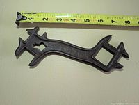 Full view of cast iron multi-tool wrench beside measuring tape