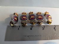 Front view of five enamel Canadian Military Engineers lapel pins with ruler for scale
