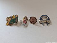 Front view of four enamel lapel pins: two angel figures, round stocking design, blue bow tie