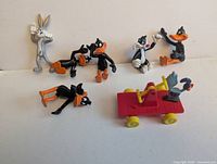 Group shot of seven Looney Tunes figurines including Bugs Bunny, four Daffy Duck, Sylvester, Road Runner on red cart