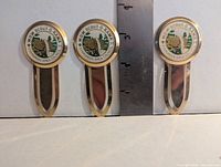 Three identical gold-tone metal bookmarks with enamel Scout-O-Rama crests shown beside ruler for scale
