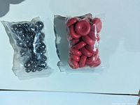 Two sealed plastic bags, left contains metallic silver-tone round beads, right contains red disk beads