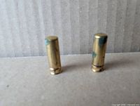 Two brass-tone miniature lipsticks standing upright showing finish wear