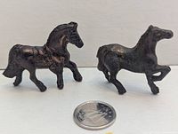 Both miniature bronze-tone horse figurines next to coin for scale