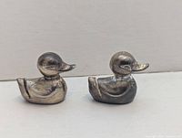 Two small metal duck figurines side by side showing profile and slot on back