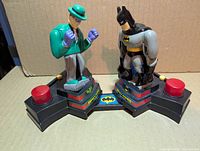 Front view of game showing Batman and Riddler figures on bases with red buttons