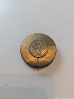 Front of brass compact showing floral engraving and patina