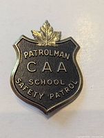 Front of shield-shaped CAA School Safety Patrol badge showing lettering and maple leaf
