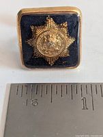 Single cufflink beside ruler showing size and badge detail