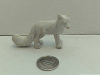 Front side of white resin arctic fox figurine with coin for scale