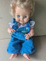 Front view of Reliable Canada doll wearing blue corduroy overalls, showing face and eyes