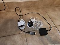 Two Blink Indoor cameras with cables and power adapter on tiled floor