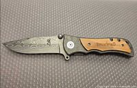 Knife open showing Damascus-pattern blade and wood inlay handle
