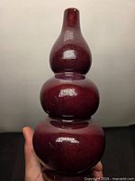 Full view of triple-gourd burgundy porcelain vase held in hand