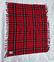 Full view of red, black and white plaid throw with fringe