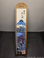 Full view of vertical plaque illustrating Mount Fuji scene on wooden backer with calligraphy and hanging slot