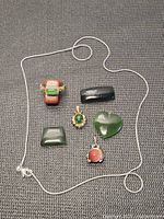 All jewellery items laid out on textured surface including chain, ring, pendants, loose stones