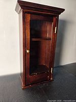 Front view of wooden wall cabinet showing glass door, brass knob, shelf