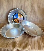 All three silver-tone fluted pie pans standing and lying to show edges and interiors