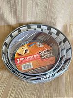 Top view of nested, plastic-wrapped three-piece springform pan set with Baker's Secret packaging insert visible