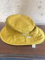 Angled exterior view of yellow Tilley bucket hat showing brim, side eyelets and brand tag