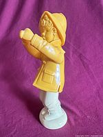 Full side view of assembled figurine showing yellow raincoat boy atop stand