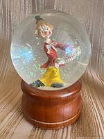 Front view of clown snow globe showing figure and wood base