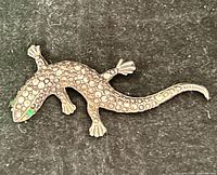 Front view of gold-tone lizard brooch showing texture and green rhinestone eyes