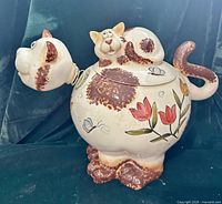Front view of cat-shaped cookie jar showing floral painting, brown patches and kitten lid