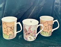 Front view showing three mugs: two ginger kitten designs and one floral cat design