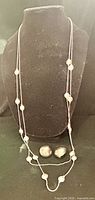 Necklace displayed hanging on bust with earrings below
