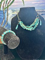 Full set displayed: necklace on bust, bracelet on roll, earrings on surface