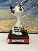 Front view showing cat figurine, plaque text, colors, and overall condition