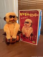 Toy seated on brown plastic barrel beside original box