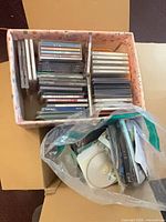Box containing inner carton of stacked jewel case discs and bag of loose discs