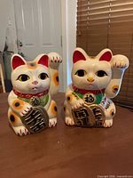 Front view of both ceramic Maneki Neko coin banks showing color, kanji plaques and overall condition