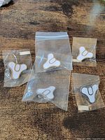 Front view of five Destiny Tricorn enamel pins in bags