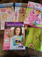 All items laid out: two sticker kits, sew-on transfer package, My Little Pony book and folded playmat