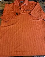 Full view of orange polo shirt showing front, collar, placket, embroidered logo and overall condition