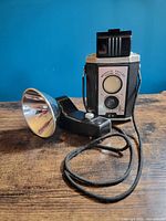 Front view of Brownie Reflex camera with flash unit attached by cord
