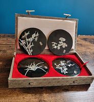 Open presentation box showing four black lacquer coasters with mother-of-pearl bamboo and floral designs