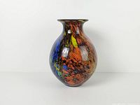 Front view of bulbous vase showing orange, yellow, blue confetti and gold leaf on cobalt base