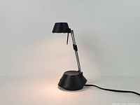 Full view of black high-intensity desk lamp showing base, telescoping chrome arm, shade, and power cord