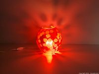 Lamp illuminated showing red glow and white floral pattern, cord and switch visible