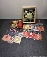 Lot overview showing kokeshi doll, framed gold-foil temple art, paper kimono charms in bags, straw sandal charms