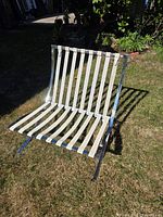 Front angled view of chrome lounge chair frame with cream leather straps on grass