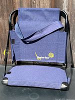 Front view of folded blue Bleacher-Back stadium seat showing logo and carry strap